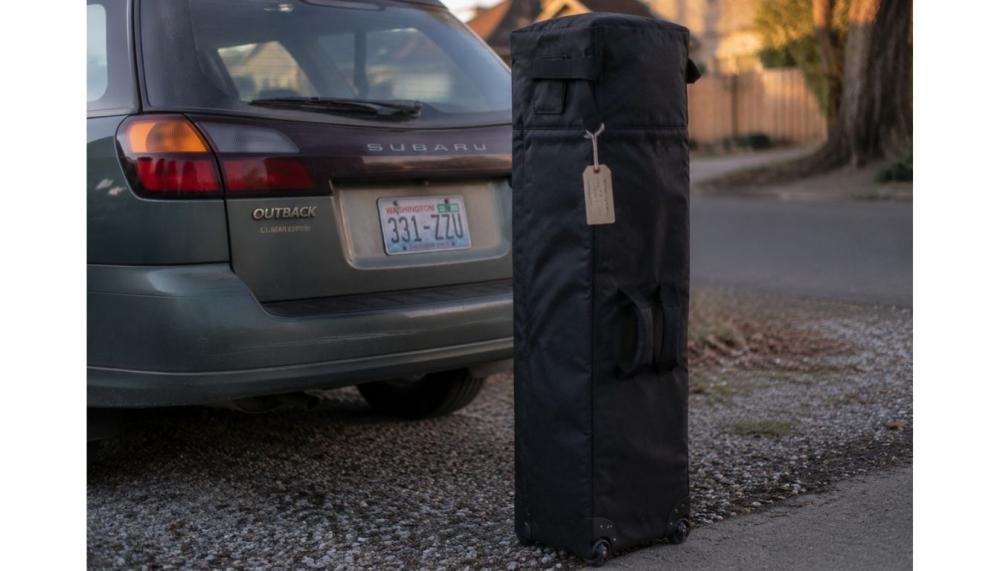 A durable black wheeled transport bag containing a packed canopy tent